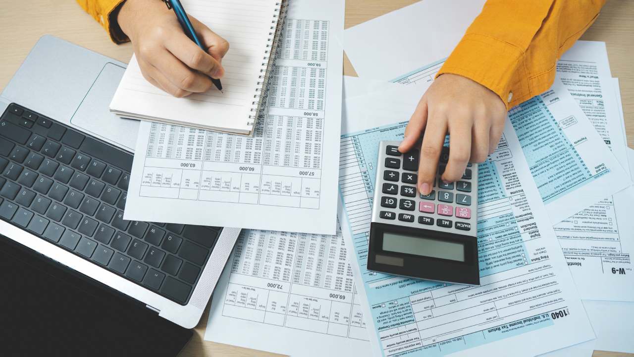 A person using a calculator and taking notes on financial documents with a laptop—illustrating how to prepare for tax time as a business owner.