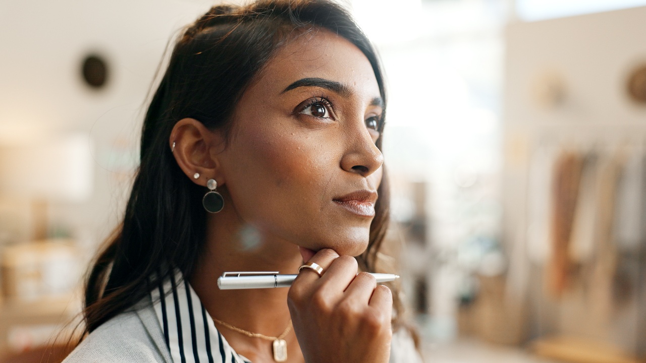 Woman thoughtfully holding a pen in a bright office space, reflecting on goals and decisions — representing financial planning tips for the year ahead.