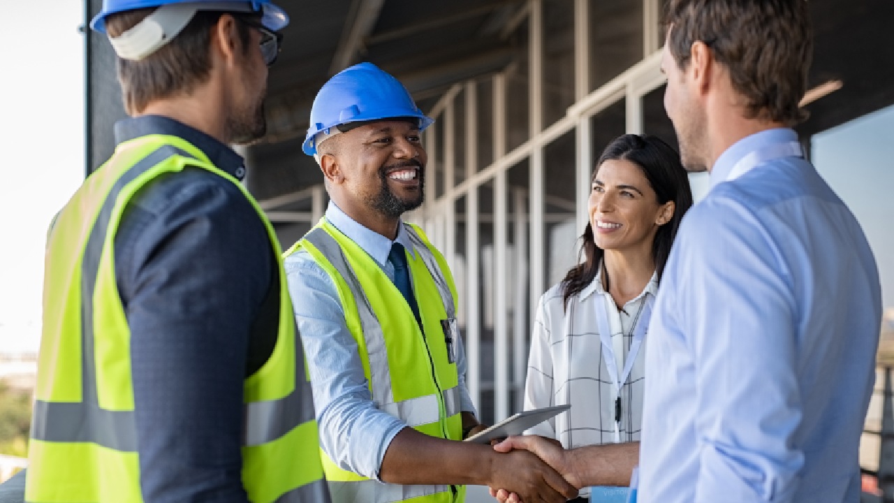 Professional meeting on a construction site with workers and advisors shaking hands, representing bookkeeping for tradies and financial collaboration on the Central Coast